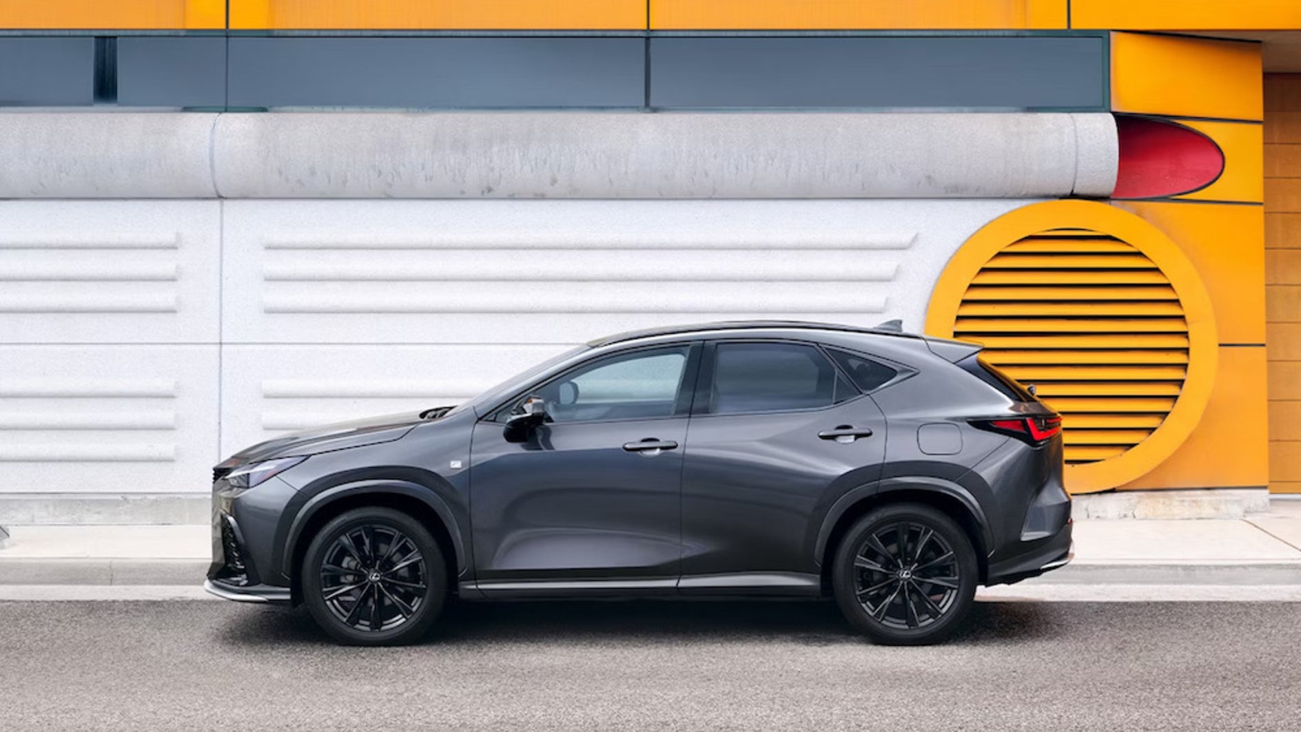 A gray 2026 Lexus NX parked in front of a concrete wall painted partially bright yellow