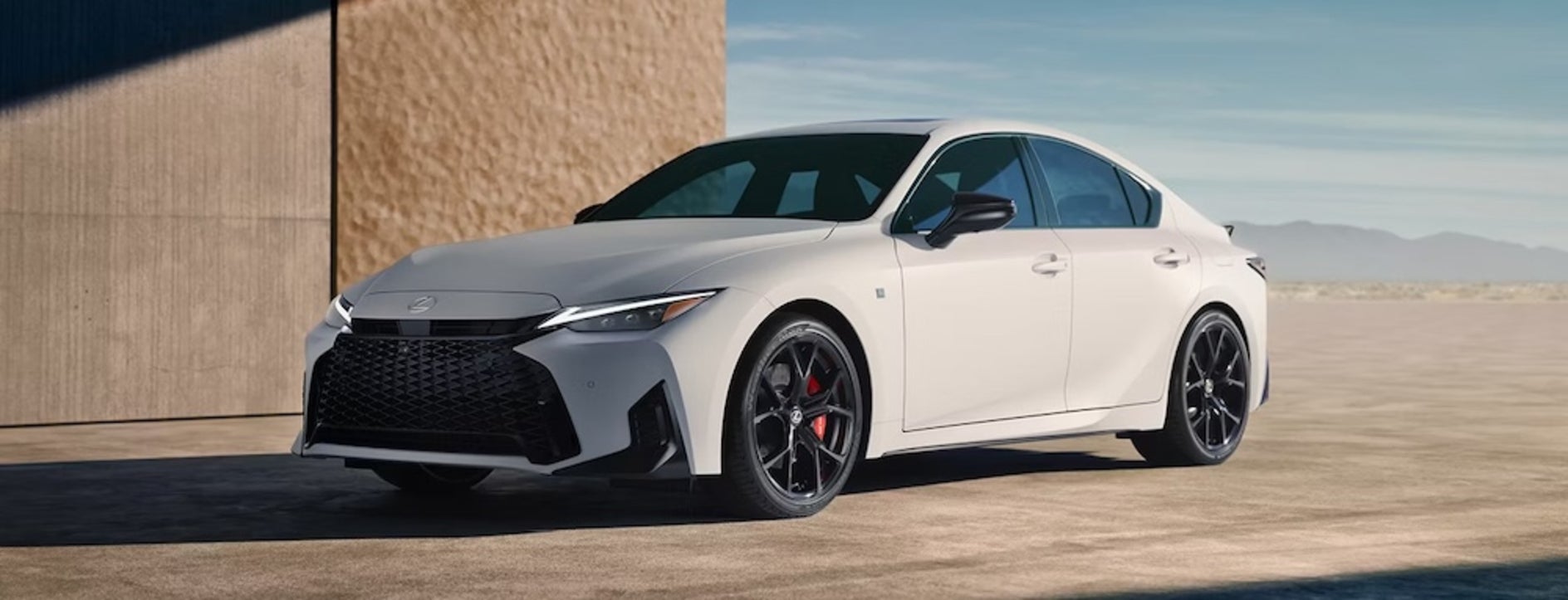A white 2026 IS F Sport parked beside a building with a desert in the background